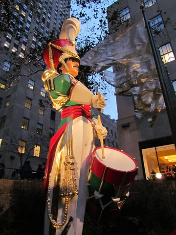 A statue of a man playing drums in front of buildings.