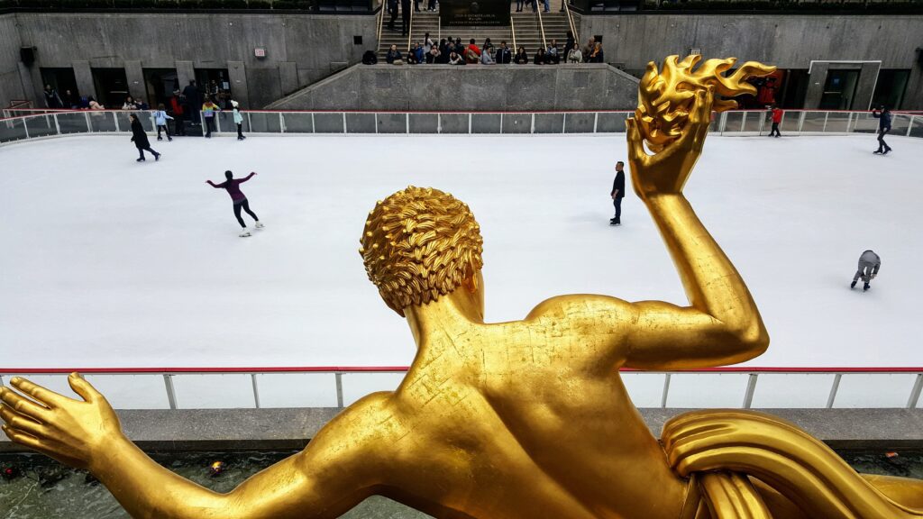 A statue of a man in gold sitting on top of an ice rink.